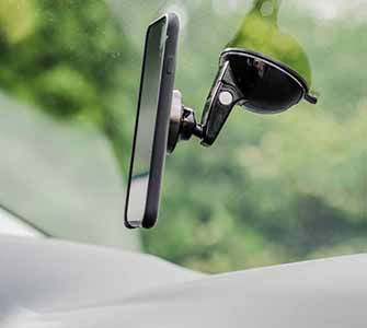 En smartphone sidder i en mobiltelefonholder på indersiden af et bilvindue. Udenfor er frodig grøn vegetation synlig i et slør.